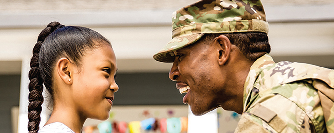 Father and young daughter facing one another. The father is wearing military fatigues