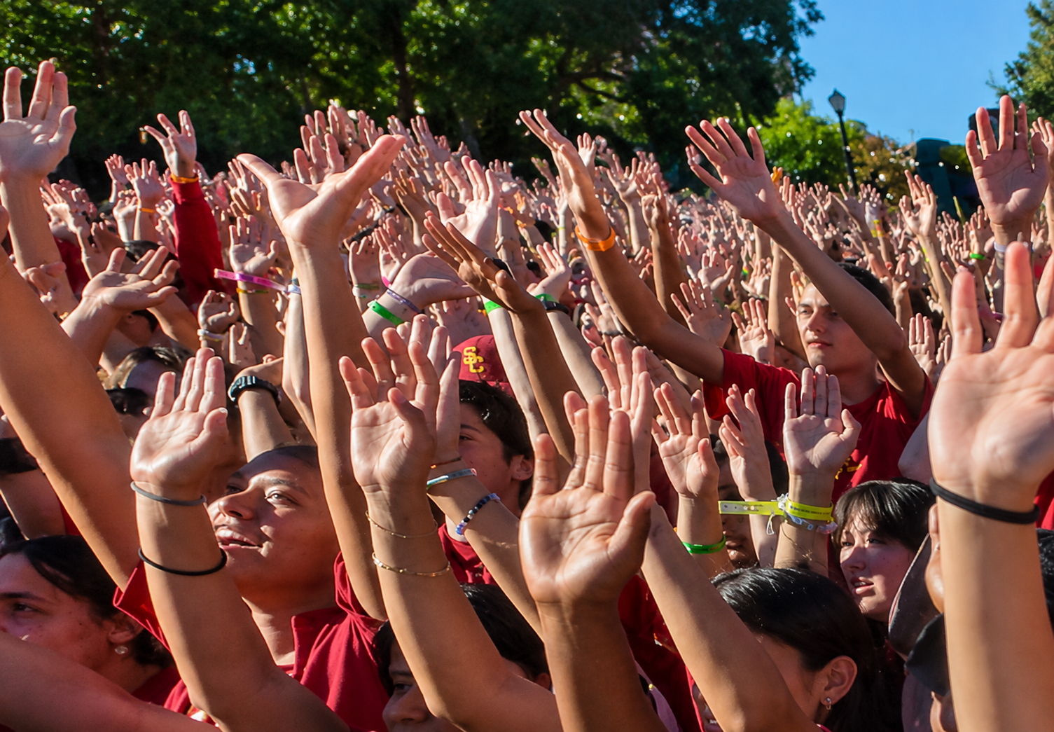 Large crowd of people raising their hands during an outdoor event on the USC campus.