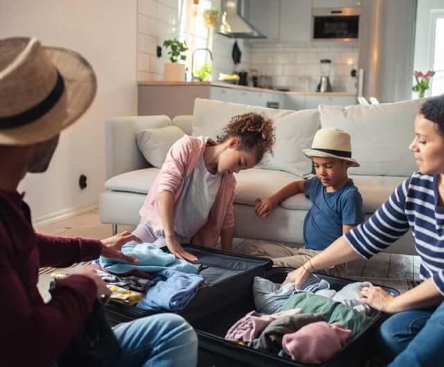 Family of four packing suitcases on a living room floor