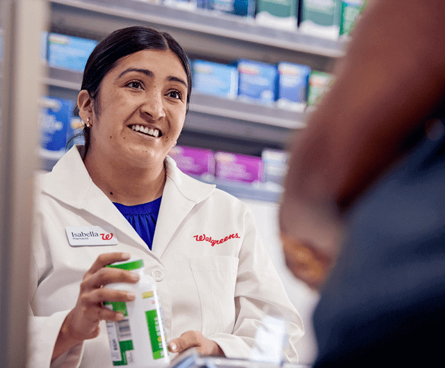 Smiling pharmacist handing customer bottle of pills