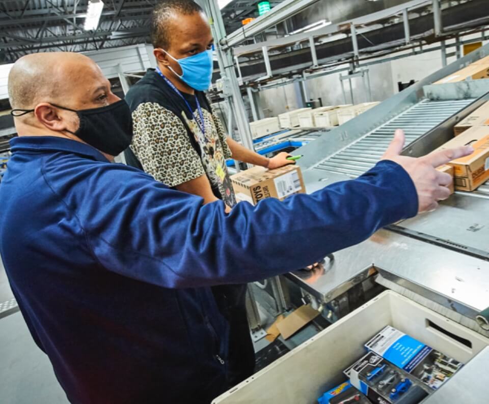 Two employees working with a sorting machine in warehouse