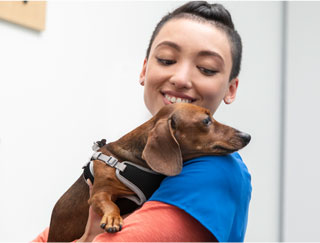 Banfield tech in blue shirt smiling at dog in her arms