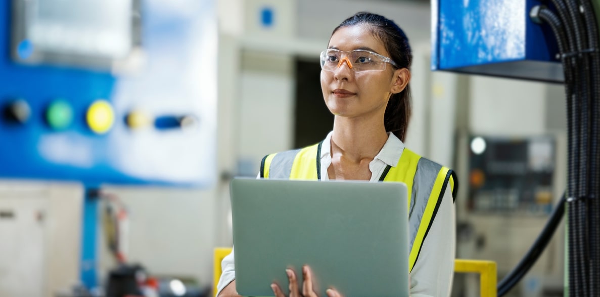 A woman in a safety vest holding a laptop, ready to work in a secure environment