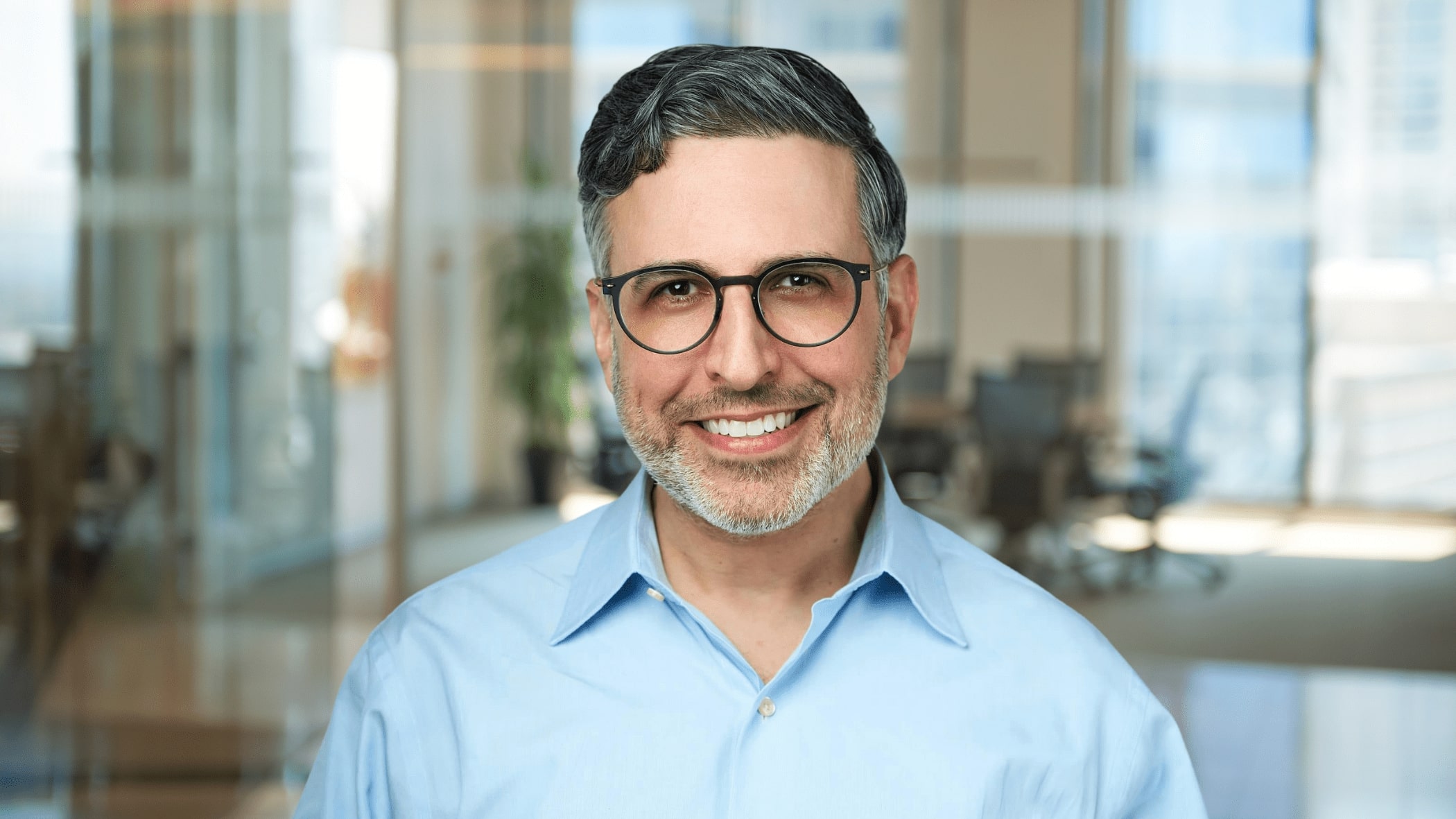 A smiling man wearing glasses and a blue shirt