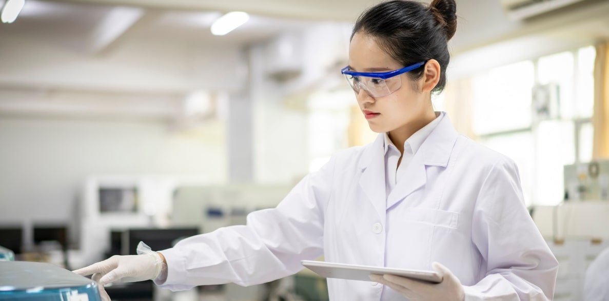 A woman in a lab coat and glasses holding a tablet