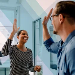 A man and woman in an office celebrate success with a high five.