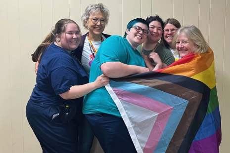 Group of people hugging and wrapped in large pride flag