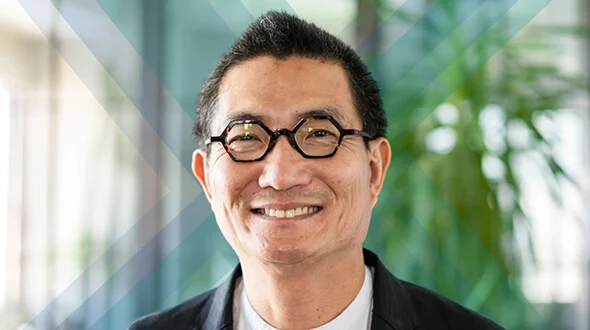 A smiling man wearing glasses and a black suit