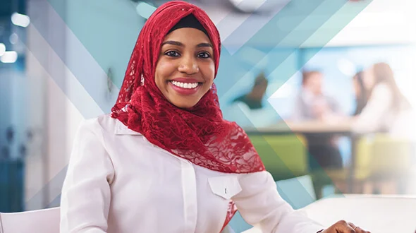 A woman wearing a red hijab and a white blouse smiles at the camera