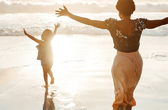 Mother and daughter running on the beach with the sun shining on the wet sand