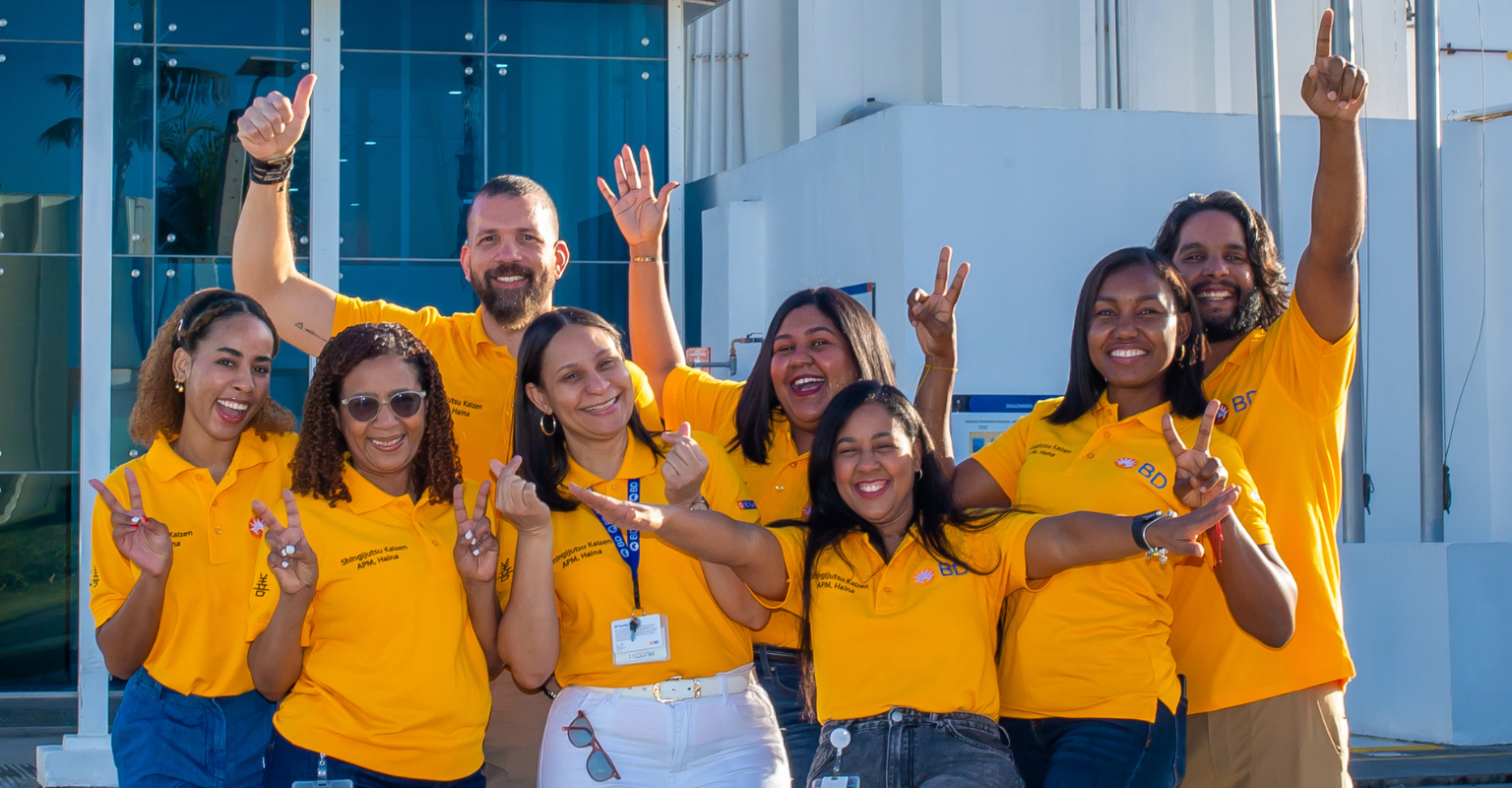 BD associates in yellow BD shirts posing outside a manufacturing facility.