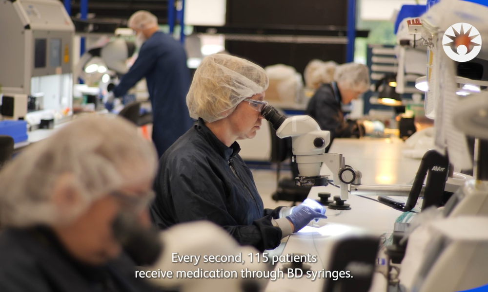 BD associate inspecting a medical device component under a microscope in a manufacturing facility.