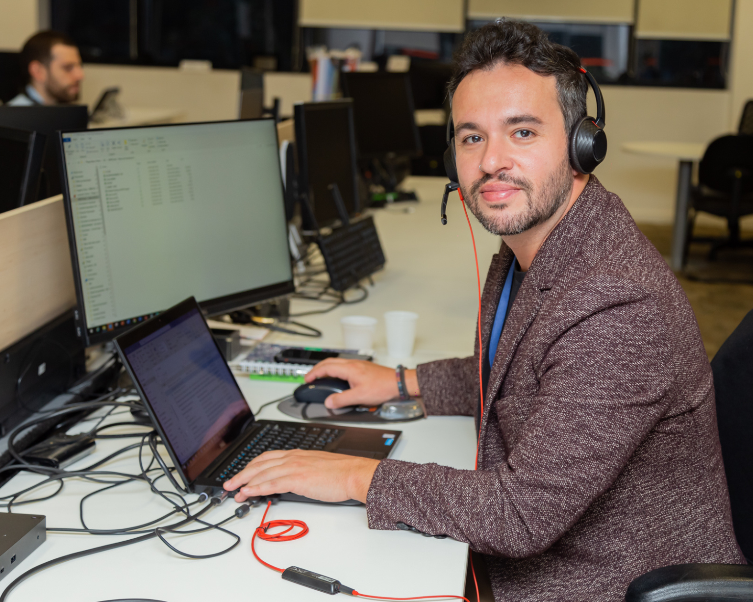 Empleado de BD usando una computadora portátil con auriculares en una oficina de BD de planta abierta.