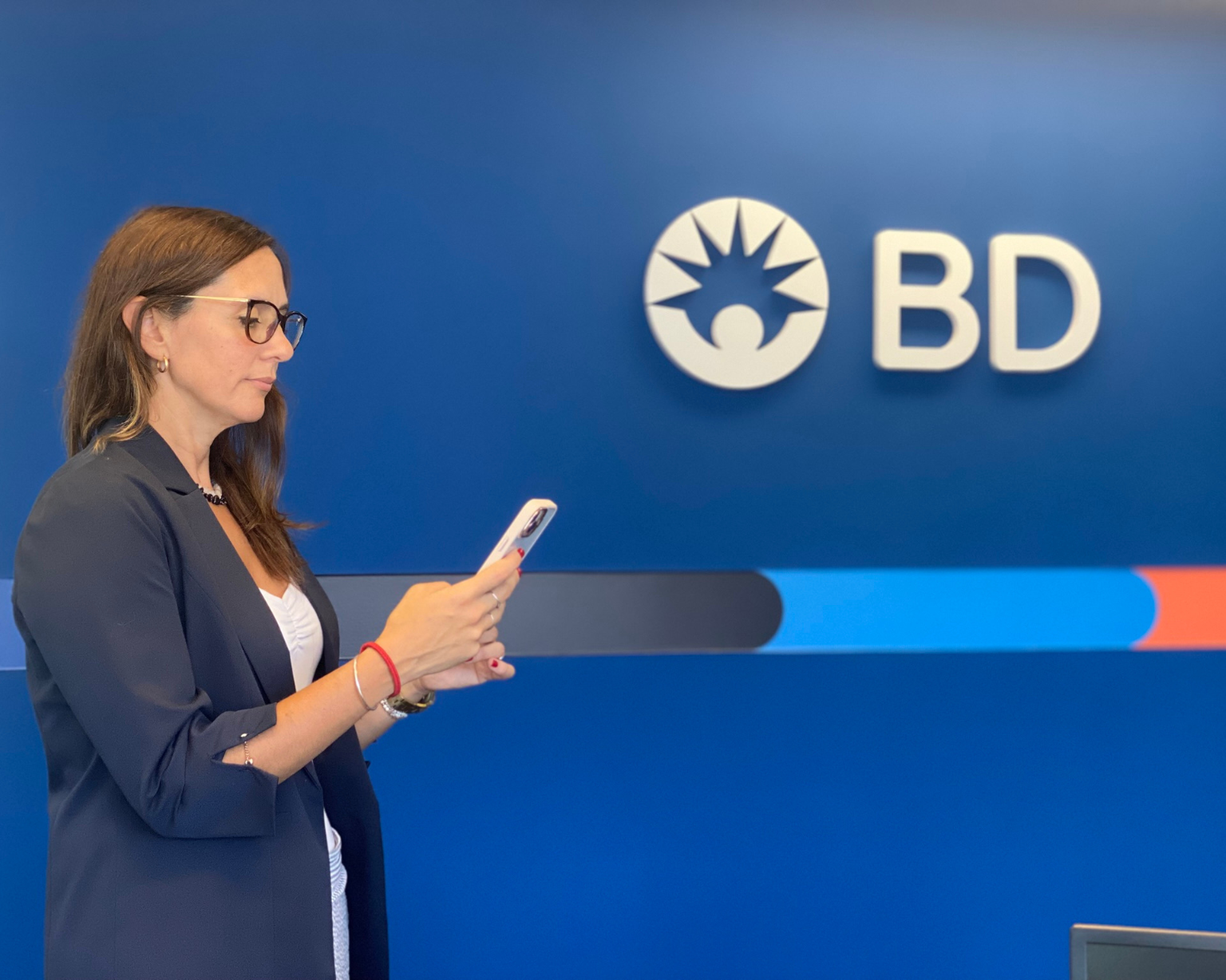 Empleado de BD usando un teléfono frente a una pared de oficina con la marca BD.