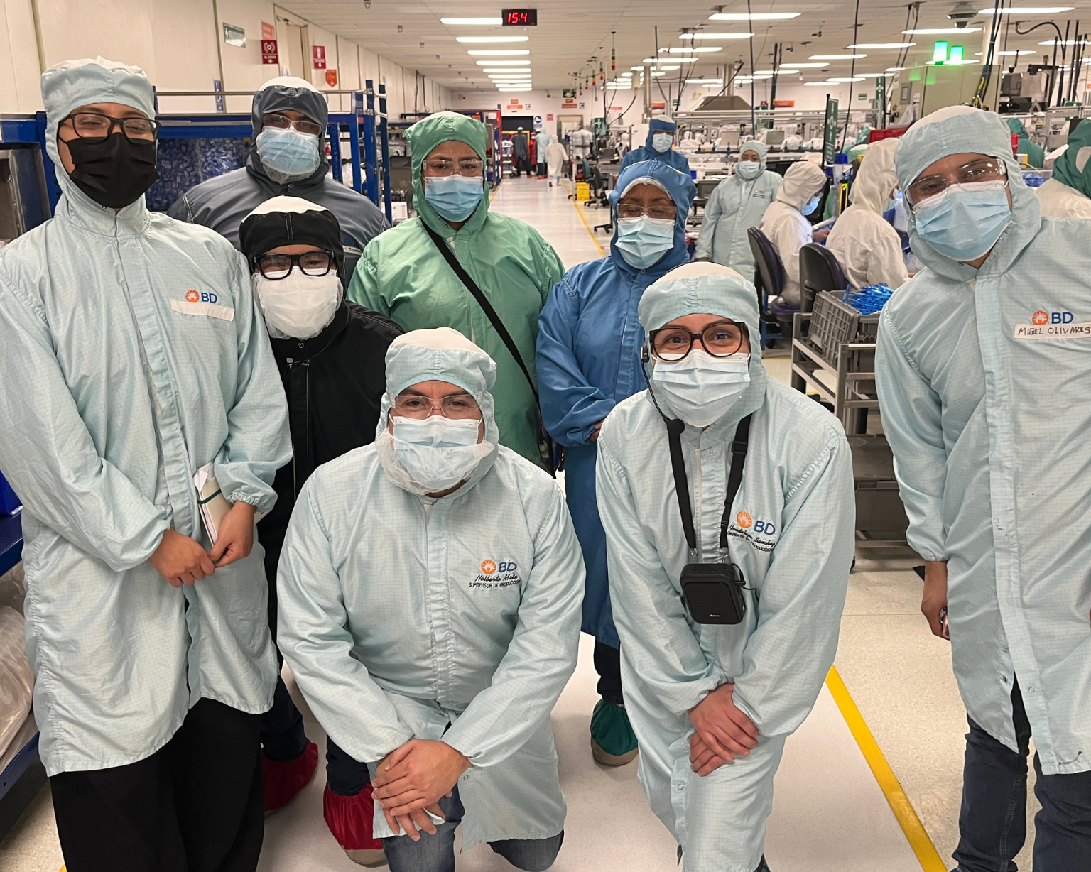 Grupo de empleados de BD con ropa de protección, de pie juntos dentro de una planta de fabricación.