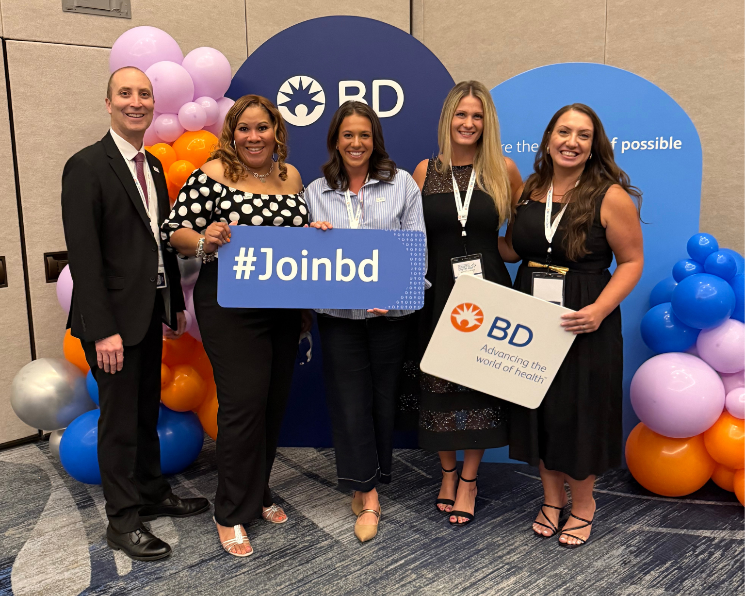 Grupo de empleados de BD sosteniendo un cartel con “#JoinBD” en un evento de reclutamiento con la marca BD.