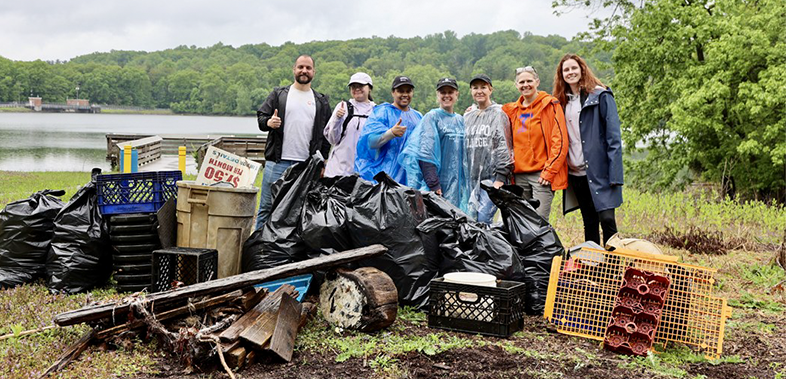 A group of individuals seated in the back of an open tractor trailer during an outdoor activity, all wearing BD-branded shirts or casual clothing. Fields and farm equipment are visible in the background.