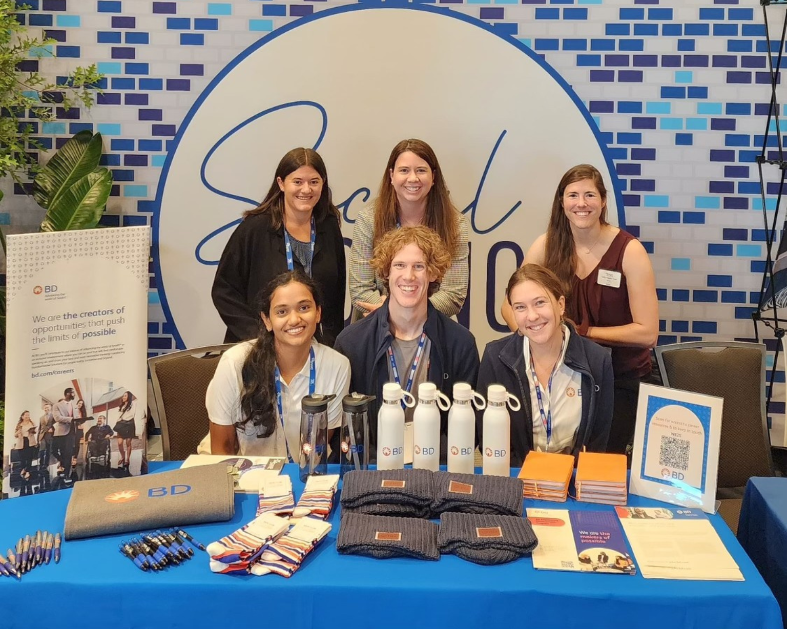 Group of BD associates at a BD-branded booth with promotional materials displayed on a table.