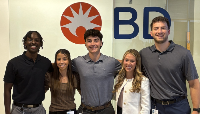 Group of early talent associates smiling in front of BD sign