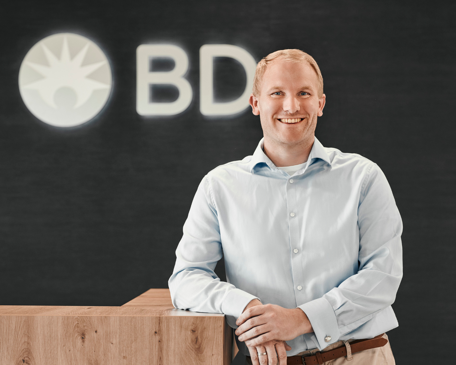 Persona de pie frente a un logotipo de BD dentro de una oficina de BD.