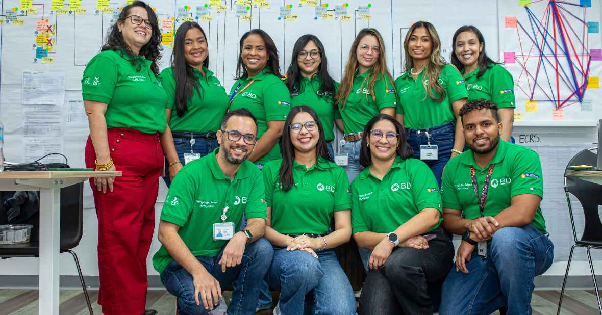 Grupo de asociados de BD posando juntos en un entorno de trabajo, frente a paneles con notas y diagramas en una sala de proyectos.