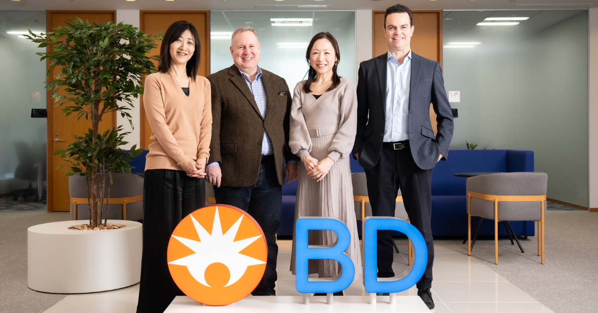 BDのアソシエイトがオフィス内で並び、BDのロゴの前で集合写真を撮っている様子。