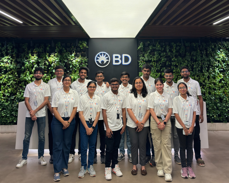 Un grupo numeroso de asociados de BD en un entorno interior, con vegetación cubriendo la pared detrás de ellos y el logotipo de BD visible.