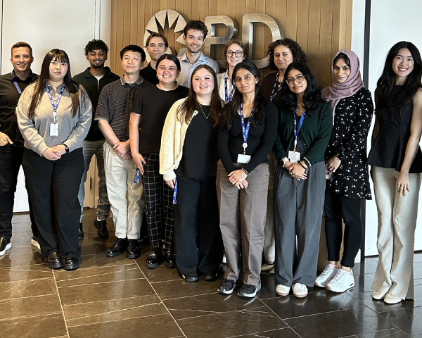 Grupo de personas de pie en el vestíbulo de una oficina de BD, con paredes revestidas de madera y un logotipo metálico de BD en exhibición.