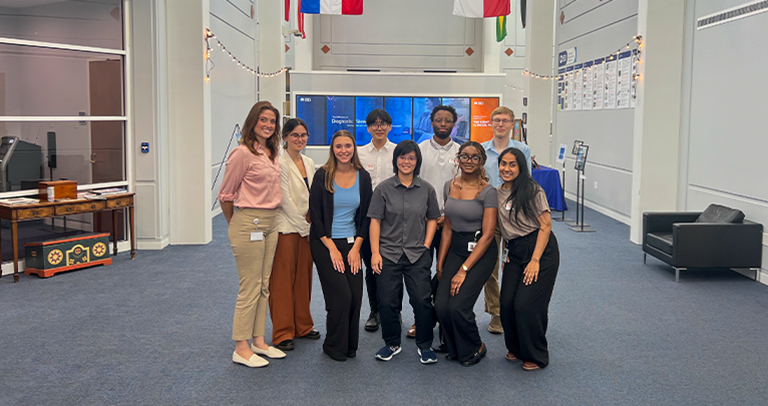 Grupo de personas de pie en un espacio de exhibición corporativo, con pantallas digitales con la marca BD, paneles informativos e iluminación decorativa.