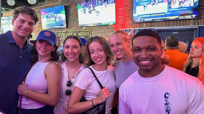 Un grupo de individuos se reunió en un bar deportivo con múltiples televisores que exhibían transmisiones deportivas y una iluminación de neón que iluminaba el espacio.