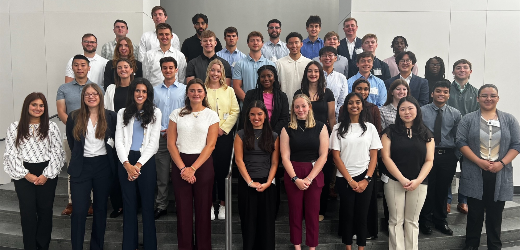 Un gran grupo de pasantes, vestidos de traje de negocios, posando juntos en las escaleras del atrio.