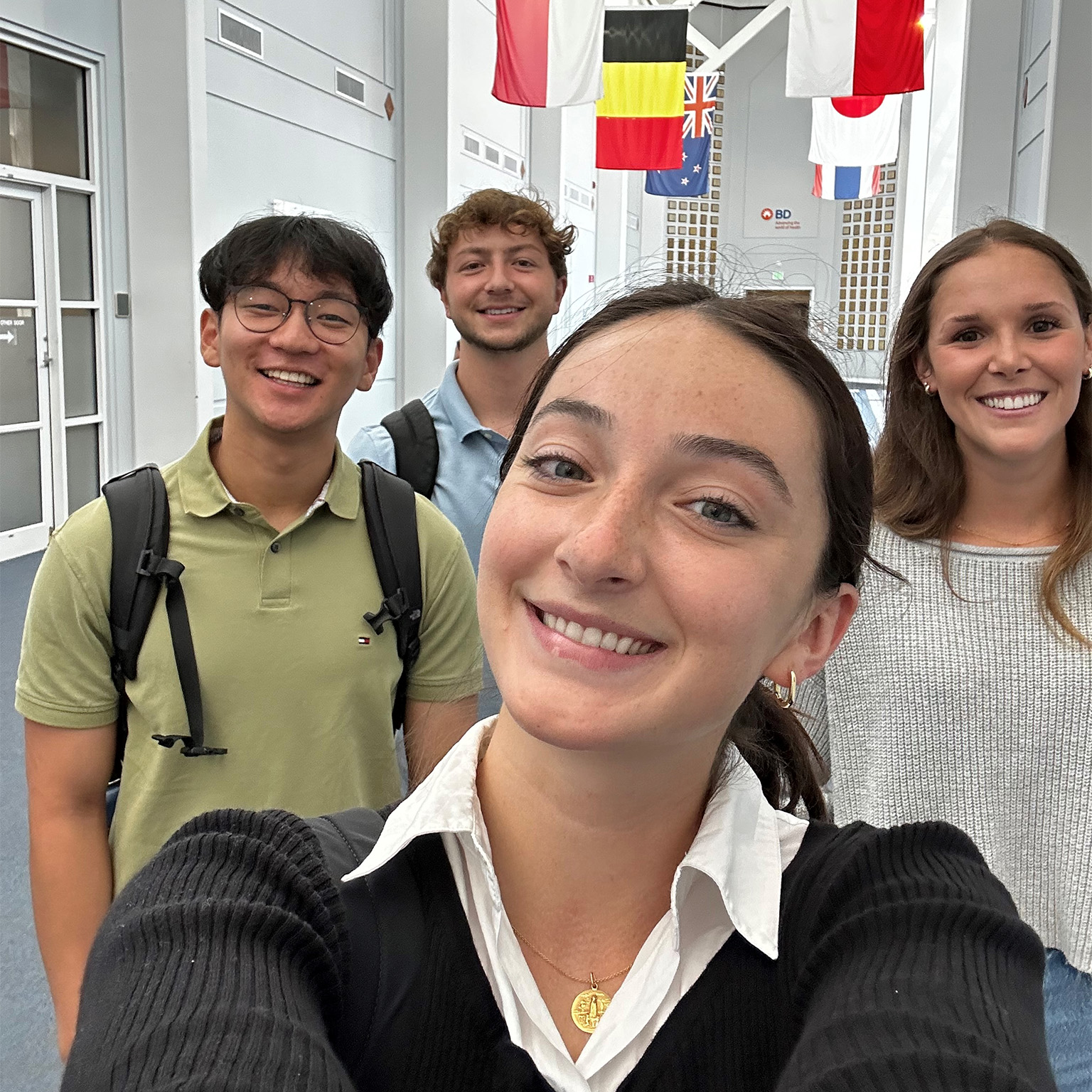 Un grupo de personas tomándose una selfie en un pasillo luminoso, decorado con múltiples banderas internacionales colgantes.