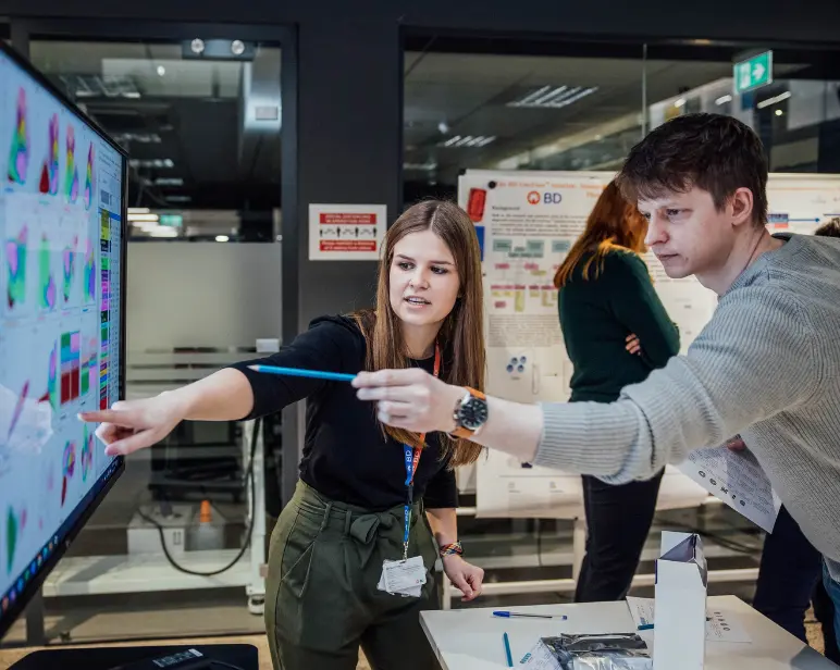 Personas colaborando en un entorno de oficina mientras revisan coloridas visualizaciones de datos en un monitor grande.