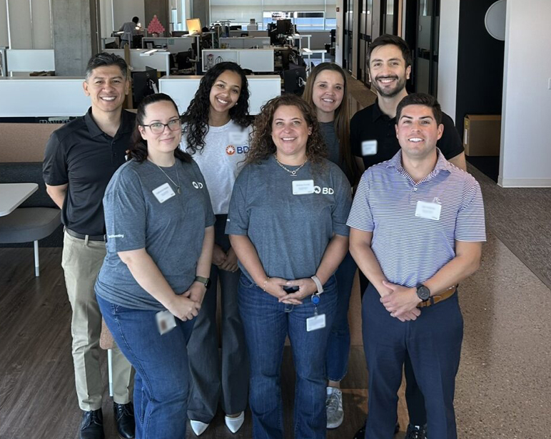 Grupo de personas de pie juntas en un espacio de oficina moderno, vistiendo camisas con el logotipo de BD.