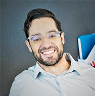 Persona con una camisa de cuello de color claro, sentada en el interior, con material de oficina visible al fondo.