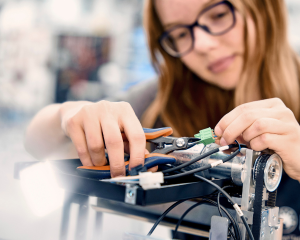 Primer plano de unas manos utilizando unos alicates para ajustar el cableado y los componentes mecánicos de un equipo técnico.