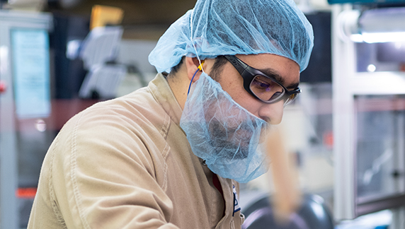 Imagen que muestra a una persona con protecci&oacute;n para la cabeza y equipo de seguridad mientras trabaja con maquinaria en una planta de fabricaci&oacute;n.