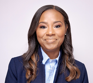 Professional studio portrait of an individual wearing a dark blazer over a striped collared shirt, photographed against a light background.