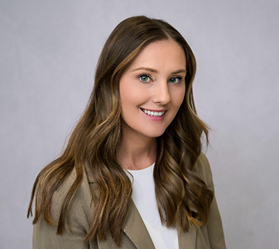 Persona con cabello largo y ondulado, vistiendo una prenda superior clara y un blazer, fotografiada contra un fondo neutro de color claro.