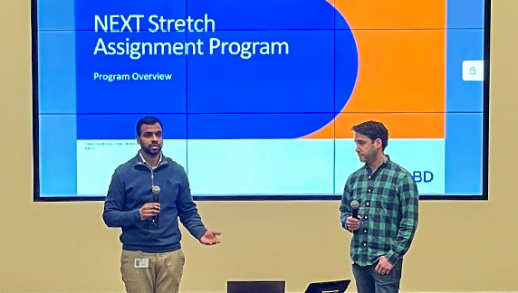 Duas pessoas segurando microfones enquanto fazem uma apresenta&ccedil;&atilde;o em frente a uma tela grande.