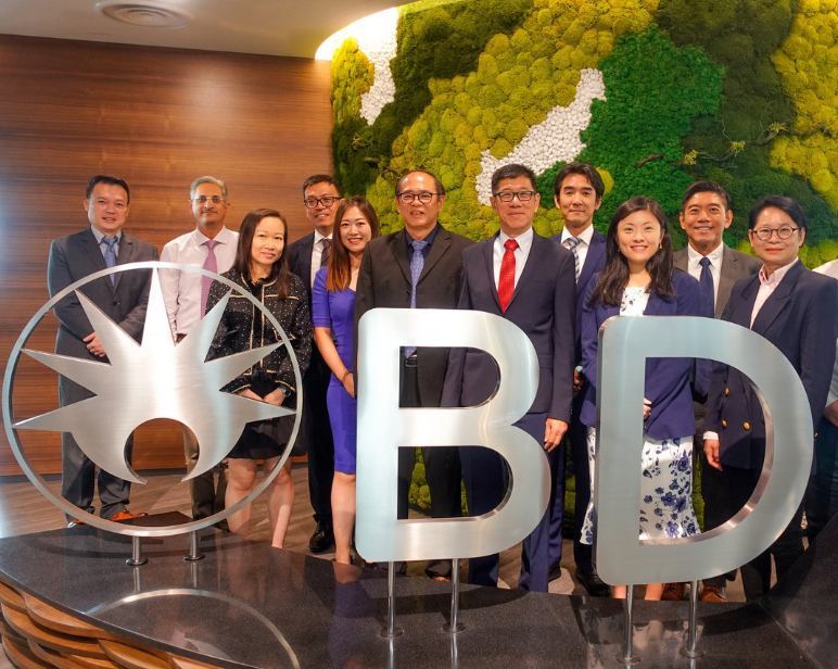 Um grupo de pessoas posou ao redor de um logotipo da BD prateado, todos vestindo trajes profissionais e sorrindo diretamente para a câmera.