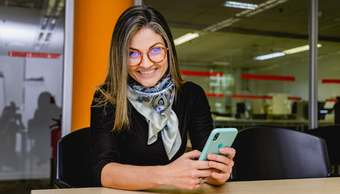 BD associate seated at a table in an office, holding a mobile phone and smiling toward the camera.