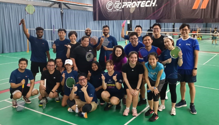 BD associates holding badminton rackets posing together on an indoor badminton court.