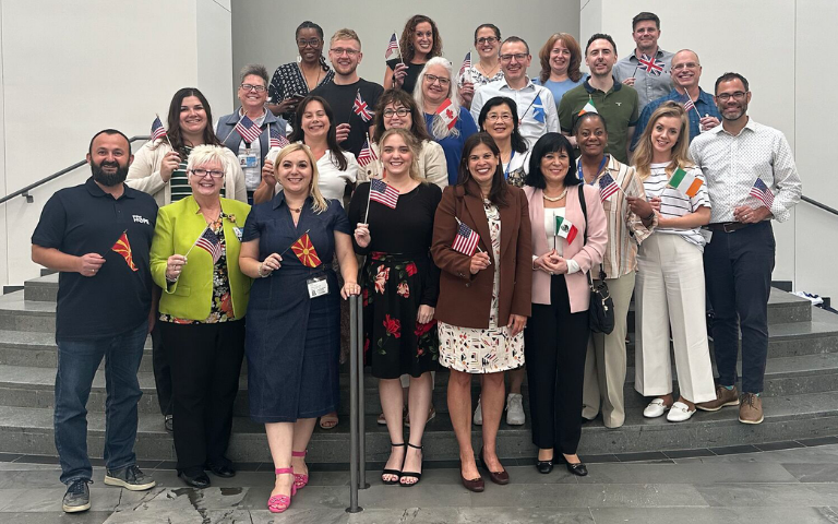 A large group of individuals standing together on indoor steps, each holding a small hand flag from various countries.