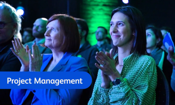 Two people clapping in the middle of a crowd, in a darkly lit room.