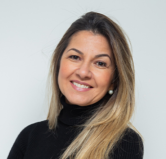 Individual wearing a black turtleneck top standing indoors against a plain light-colored background in a close-up portrait-style photograph. The individual has long hair styled to one side and is facing the camera.