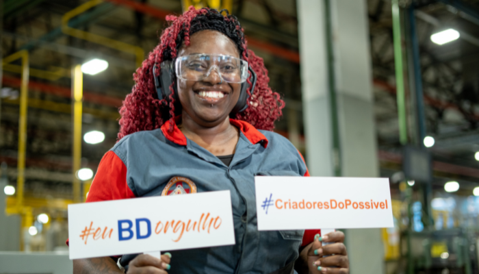 BD associate wearing safety gear holding a branded sign inside a manufacturing facility.