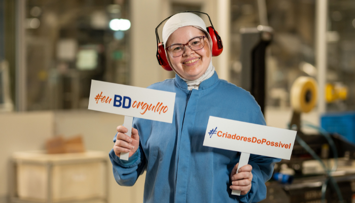 BD associate wearing hearing protection holding a branded sign in a production area.