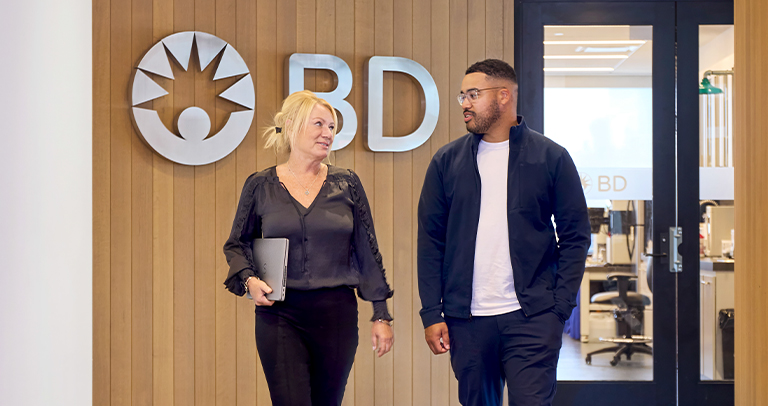 Deux associés de BD discutant dans un corridor de bureau.