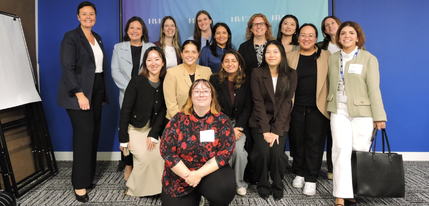 Un groupe de seize personnes posant dans une salle de conférence ou de réunion devant un arrière‑plan bleu affichant un lettrage répété.
